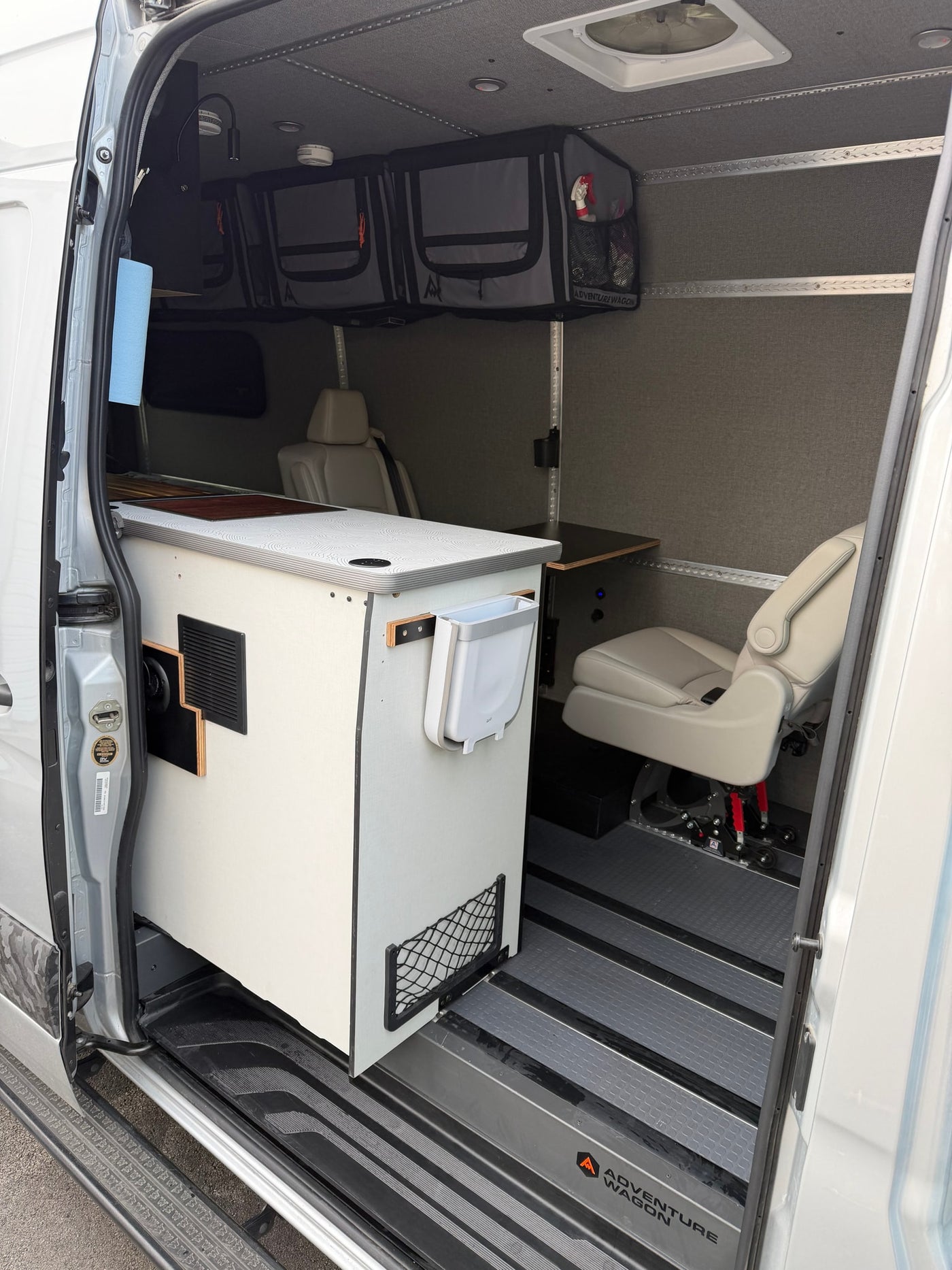 This Adventure Wagon camper van interior, ideal for an RV rental, shows a modular kitchen, storage, and swivel seat. — photo 4