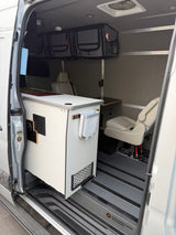 This Adventure Wagon camper van interior, ideal for an RV rental, shows a modular kitchen, storage, and swivel seat.