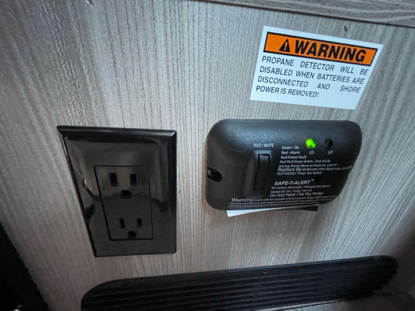 RV rental safety features: a propane/CO detector (green lights on) and an electrical outlet, with a power warning sticker.