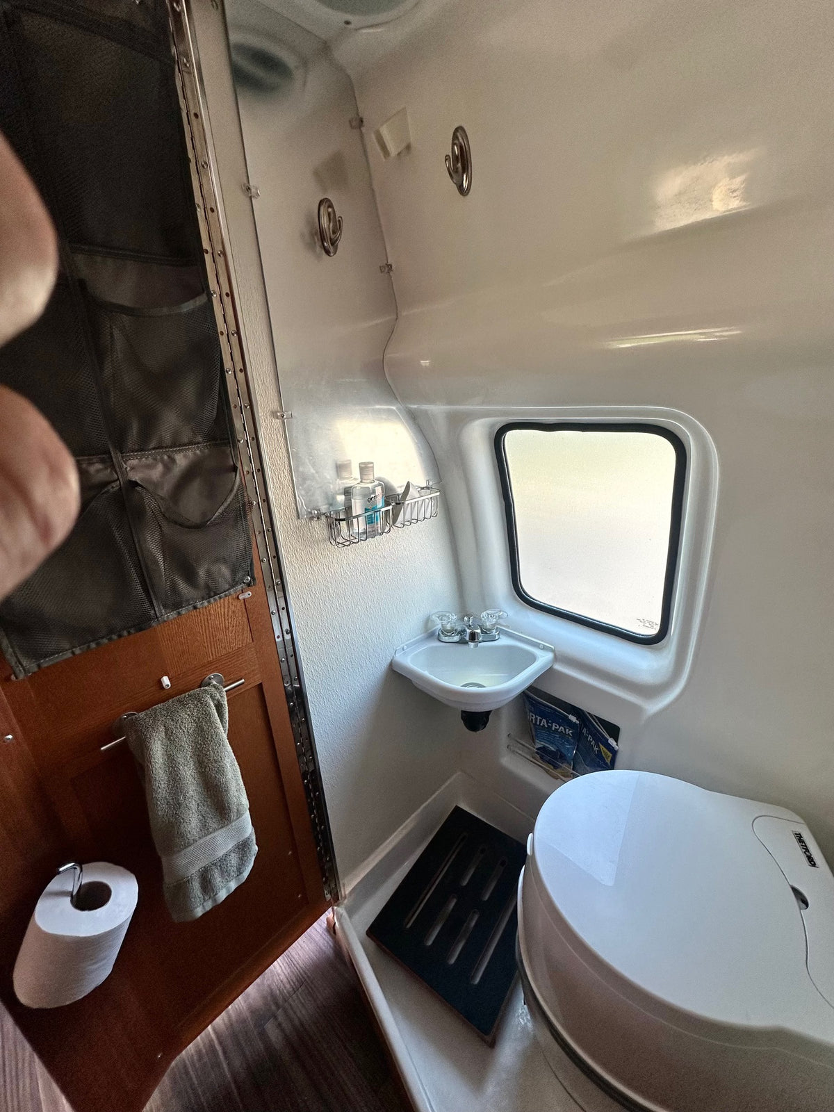 Inside an RV rental wet bath featuring a compact toilet, small sink, window, and wall storage for essentials. — photo 9