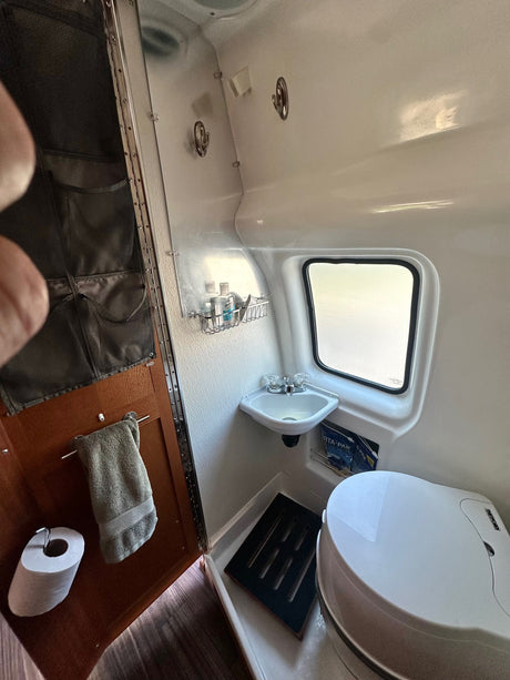 Inside an RV rental wet bath featuring a compact toilet, small sink, window, and wall storage for essentials.