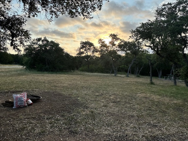 RV rental camping: serene campsite at sunset with a fire pit & picnic table in a natural setting.
