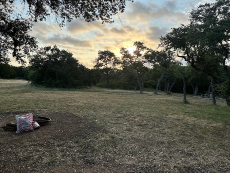 RV rental camping: serene campsite at sunset with a fire pit & picnic table in a natural setting.