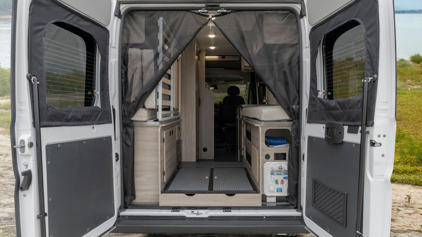 Open rear doors reveal an RV rental's camper van interior: bed, smart storage, and utility panel for comfortable mobile living. — photo 16