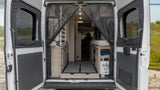 Open rear doors reveal an RV rental's camper van interior: bed, smart storage, and utility panel for comfortable mobile living.
