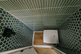 Inside an RV rental: a compact shower with green hexagonal & subway tiles, wooden mat, and a portable toilet.