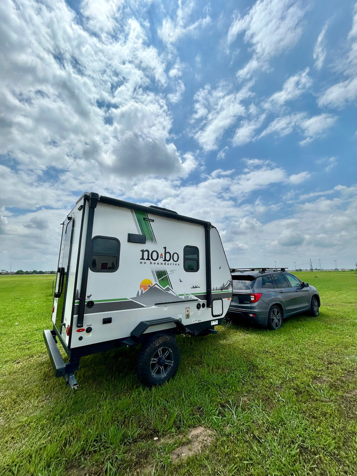 This No Boundaries travel trailer RV rental, hitched to an SUV in a grassy field under a cloudy sky, is ready for adventure.