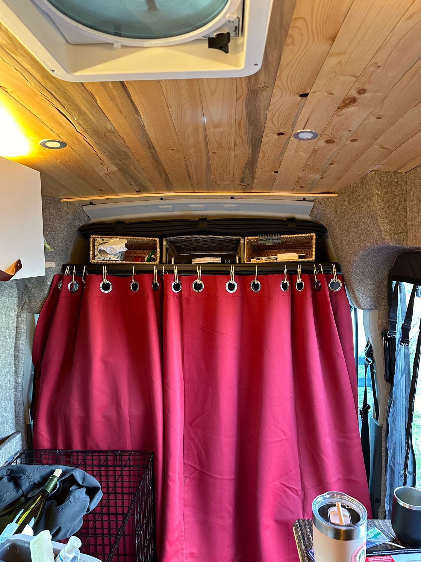 Cozy RV rental interior: wood plank ceiling, overhead storage baskets, and a vibrant red privacy curtain.