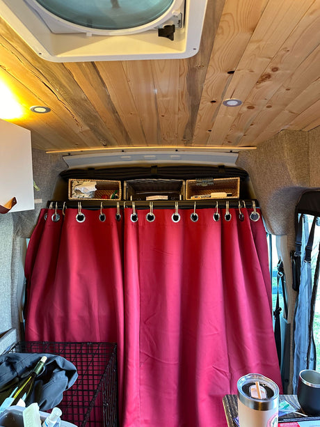Cozy RV rental interior: wood plank ceiling, overhead storage baskets, and a vibrant red privacy curtain.