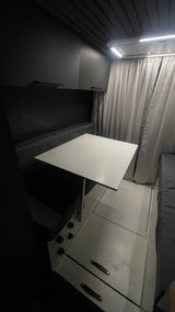 This RV rental's sleek interior features a bright white dining table, dark bench seating, and ample overhead lighting.