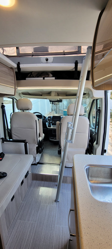A clean RV rental interior, with a kitchen, dinette, and front cabin, plus a ladder to the sleeping bunk.