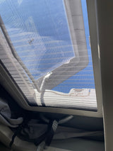 RV rental view: Sunlight streams through the roof vent screen, revealing blue sky and a small insect.