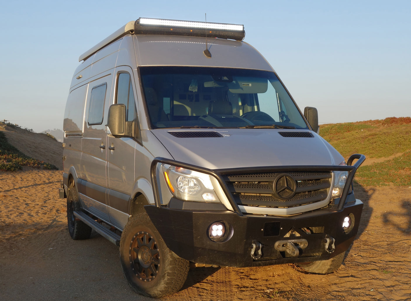 Front view of a customized, light-tan Mercedes Sprinter camper van, equipped for off-road RV rental adventures.
