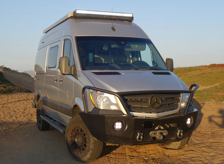 Front view of a customized, light-tan Mercedes Sprinter camper van, equipped for off-road RV rental adventures.