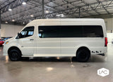 Sleek white camper van, possibly a Sprinter, showcasing its rugged tires & dark windows, ideal for an RV rental.