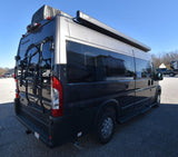 A dark gray Tellaro Class B camper van, equipped with a bike rack & awning, ready for RV rental.