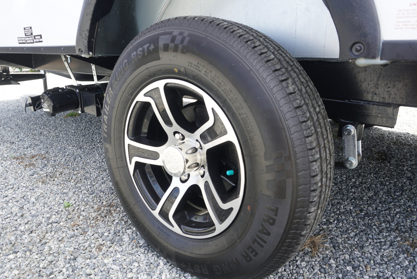 An RV rental trailer's wheel and "TRAILER KING" tire are visible, with wastewater tank connections below on a gravel lot.