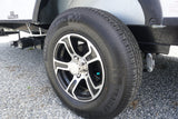 An RV rental trailer's wheel and "TRAILER KING" tire are visible, with wastewater tank connections below on a gravel lot.