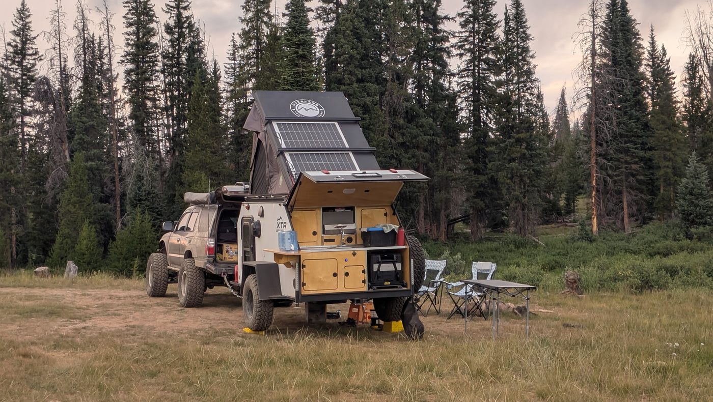 Rugged truck with an equipped overland trailer (RV rental alternative) with solar, kitchen, and roof tent in a forest. — photo 5
