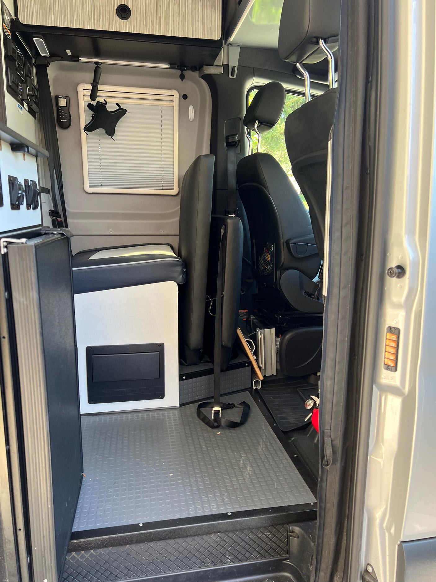 RV rental interior, from the open side door, featuring modular seating, a control panel, window, and durable flooring.
