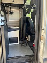 RV rental interior, from the open side door, featuring modular seating, a control panel, window, and durable flooring.