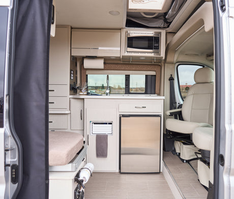 Modern rv rental interior view from the side door: kitchen, bed area, and front seats. Ready for adventures!