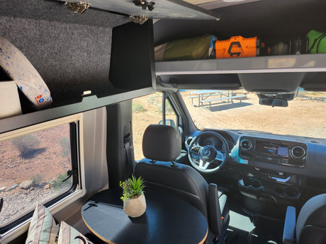 Spacious RV rental interior featuring the cockpit, overhead storage, and a cozy table, ready for desert adventures.
