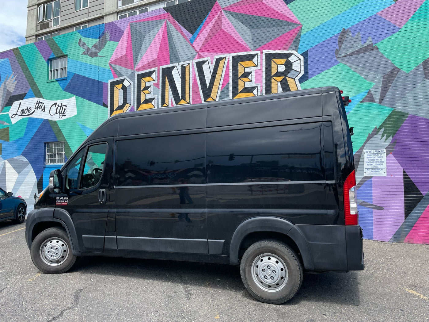  parked by a vibrant Denver mural.|Explore van life! This black Ram ProMaster camper van for RV rental reveals its cozy interior by a vibrant mural.|This **rv rental** van offers comfort! A black dog sits in the passenger seat — photo 3