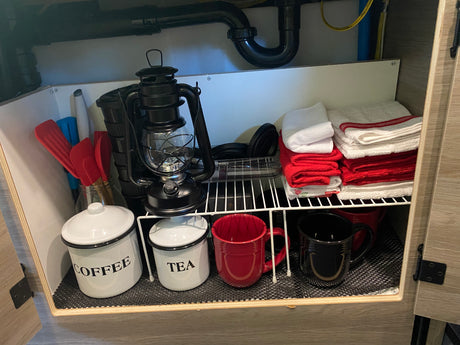 Organized RV rental cabinet with coffee/tea, mugs, lantern, utensils, and neatly folded towels, ideal for travel.