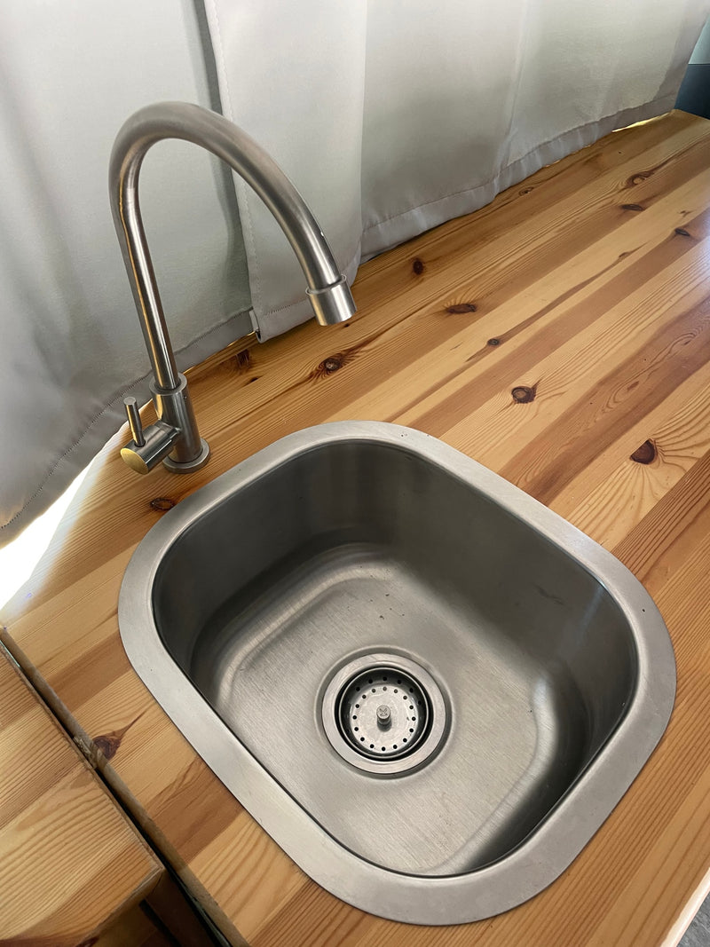 RV rental kitchen area: A sleek stainless steel sink with a gooseneck faucet on a pine wood counter, with light curtains. — photo 7