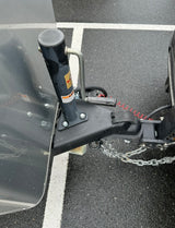 RV rental: Close-up of a travel trailer's hitch, jack, and safety chains on wet pavement, ready for towing.