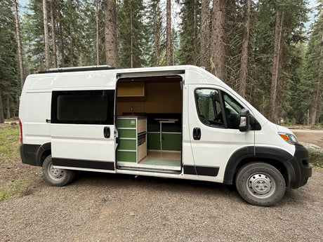 Spacious white camper van with custom green interior, parked in a pine forest, ready for your RV rental adventure.