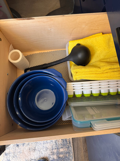 An organized RV rental kitchen drawer, showing nesting blue bowls, a ladle, paper towels, and various food storage containers.