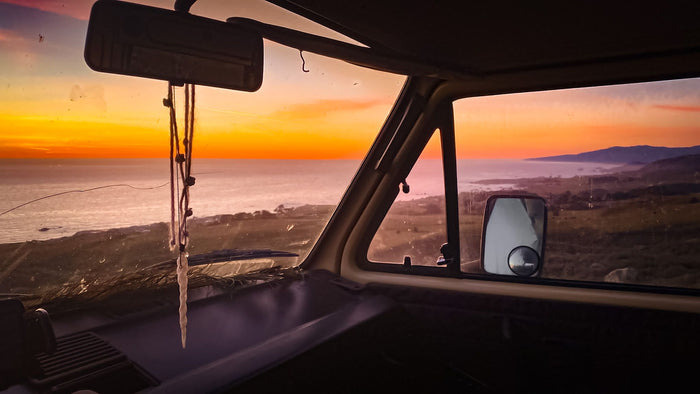 Gorgeous golden sunset over the ocean from an RV rental. View from inside a camper van on a coastal road trip.