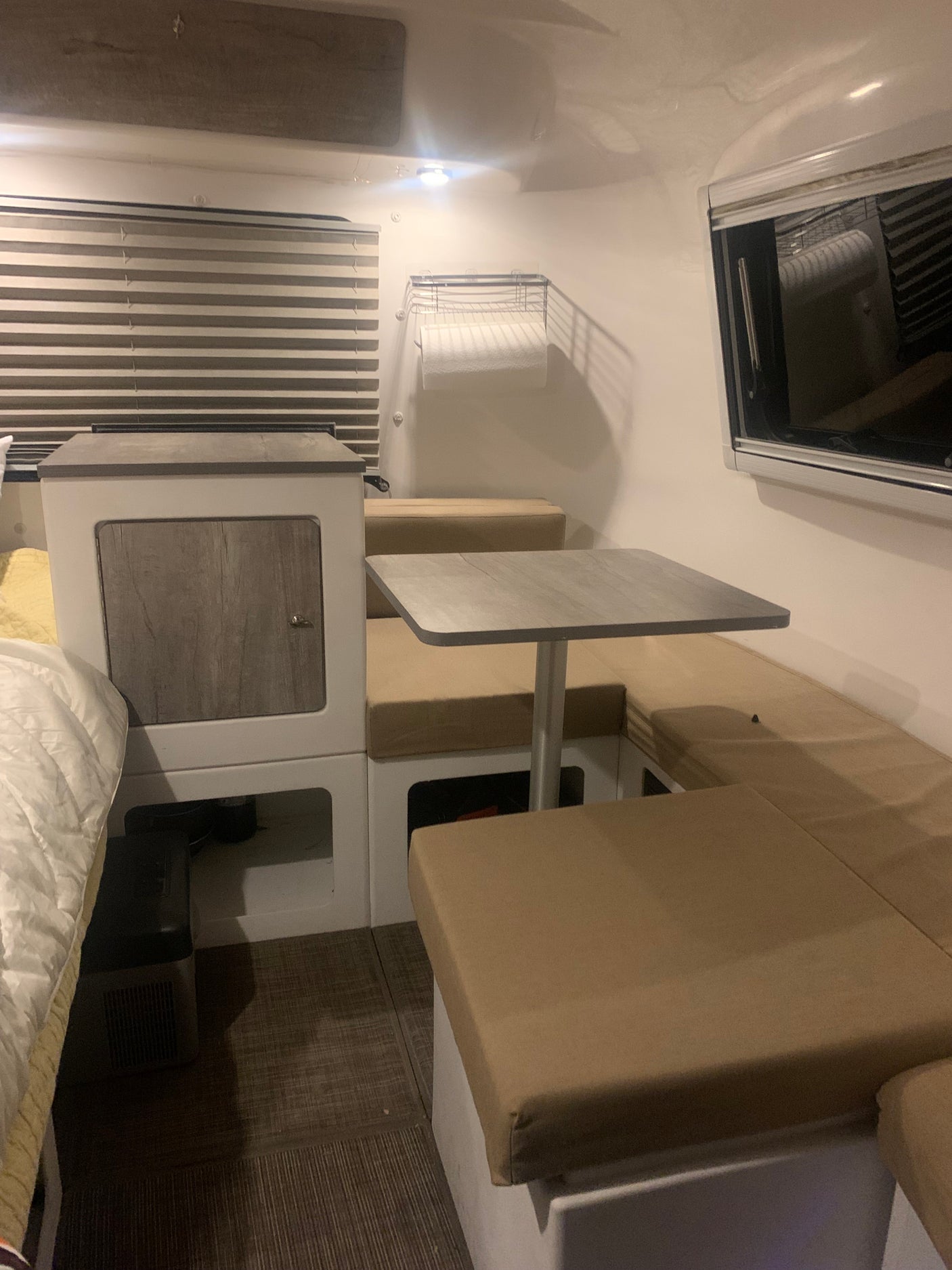 An RV rental interior features a cozy bed, dinette with table & bench seating, and smart storage for compact living.