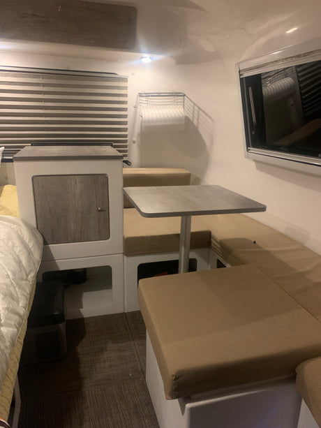 An RV rental interior features a cozy bed, dinette with table & bench seating, and smart storage for compact living.