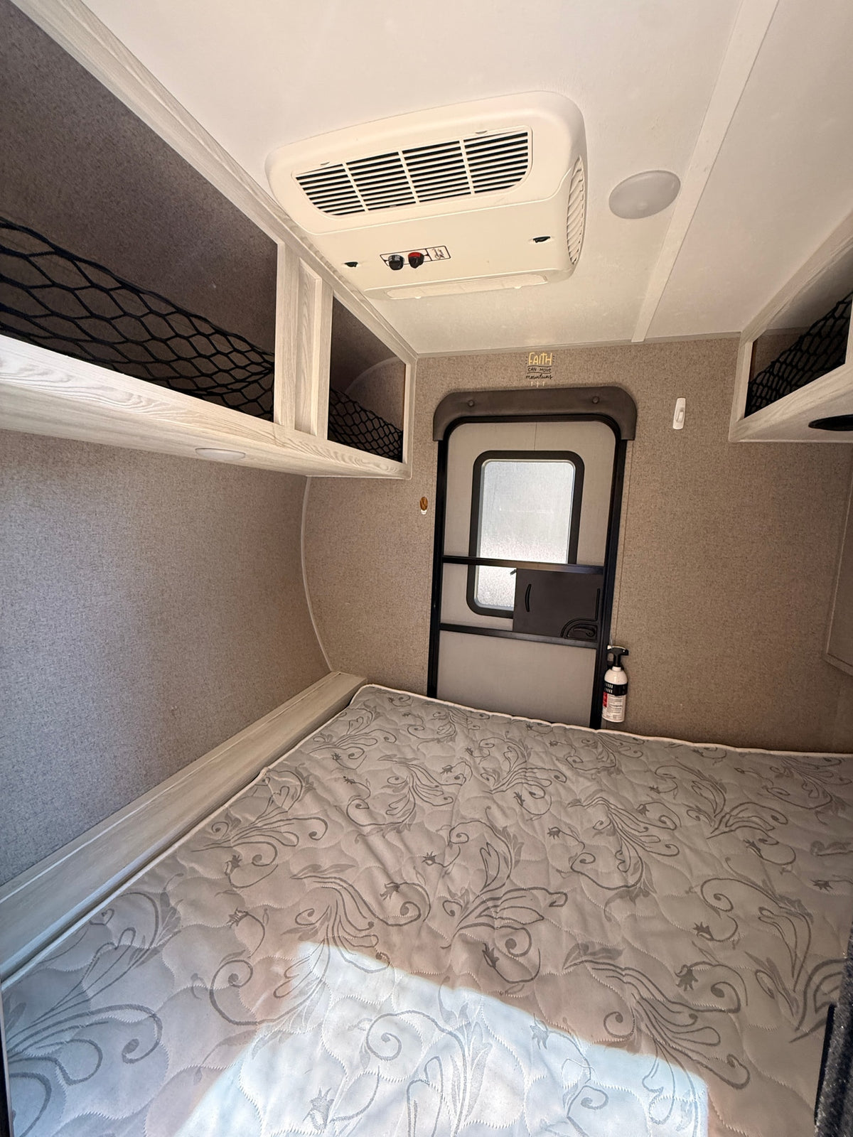 Inside this RV rental: a comfortable bedroom with a mattress, upper storage, AC, entrance door, and safety extinguisher. — photo 6
