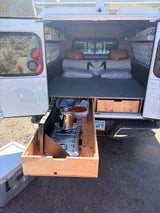 An RV rental camper reveals a pull-out kitchen with a stove and coffee pot, plus a cozy sleeping area, ready for adventure.