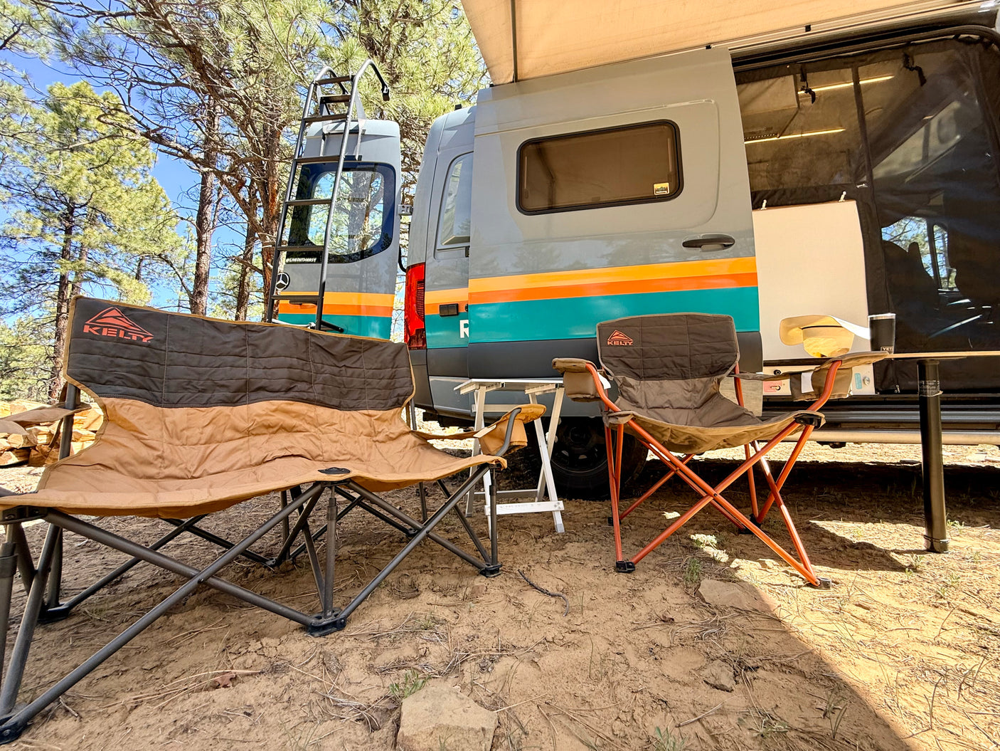 RV rental getaway: Relaxing campsite setup with two Kelty camping chairs next to a striped campervan under trees.
