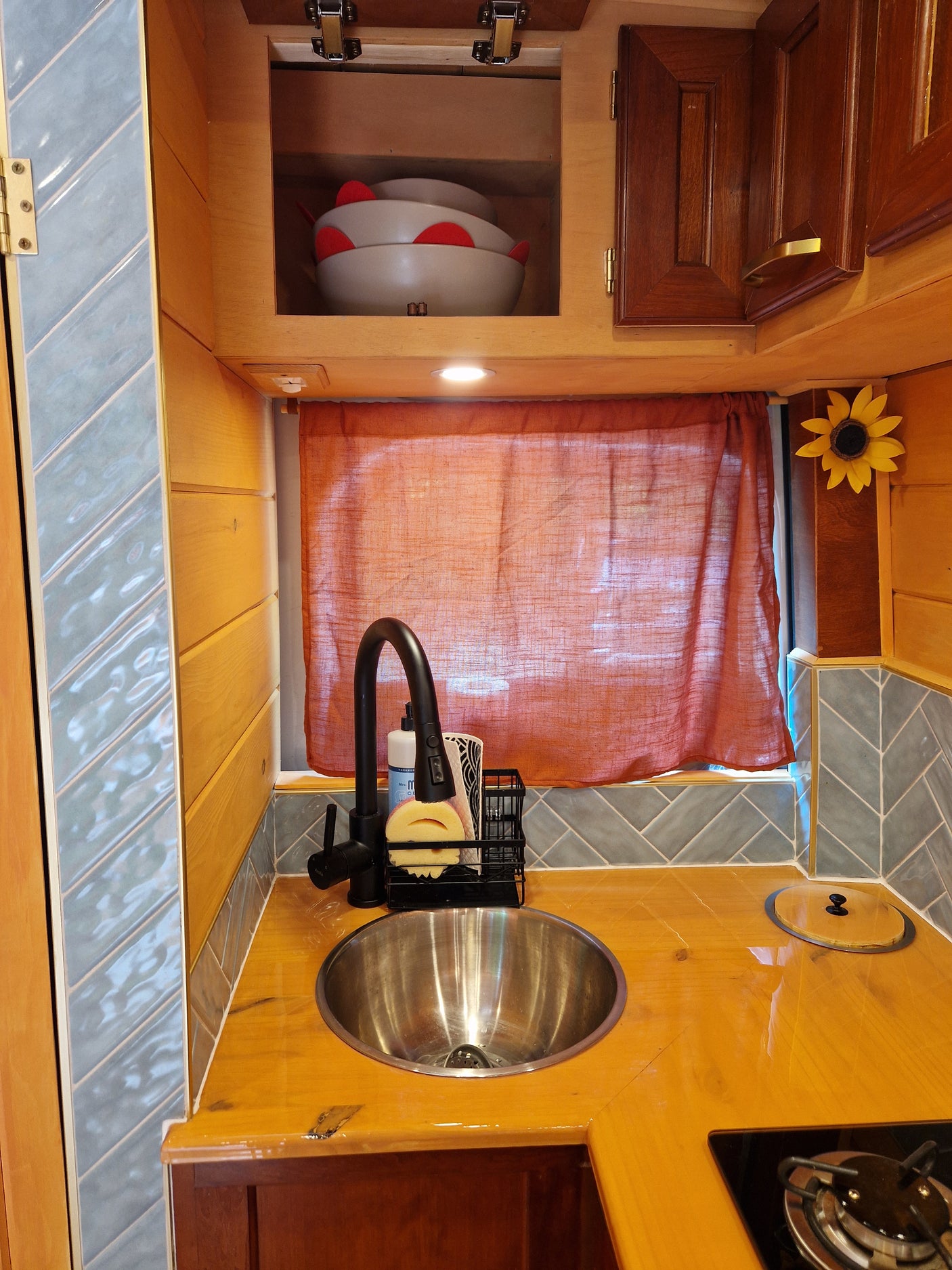 Compact RV rental kitchen with a stainless steel sink, wooden counters, and blue chevron tile backsplash. Ideal for travel.