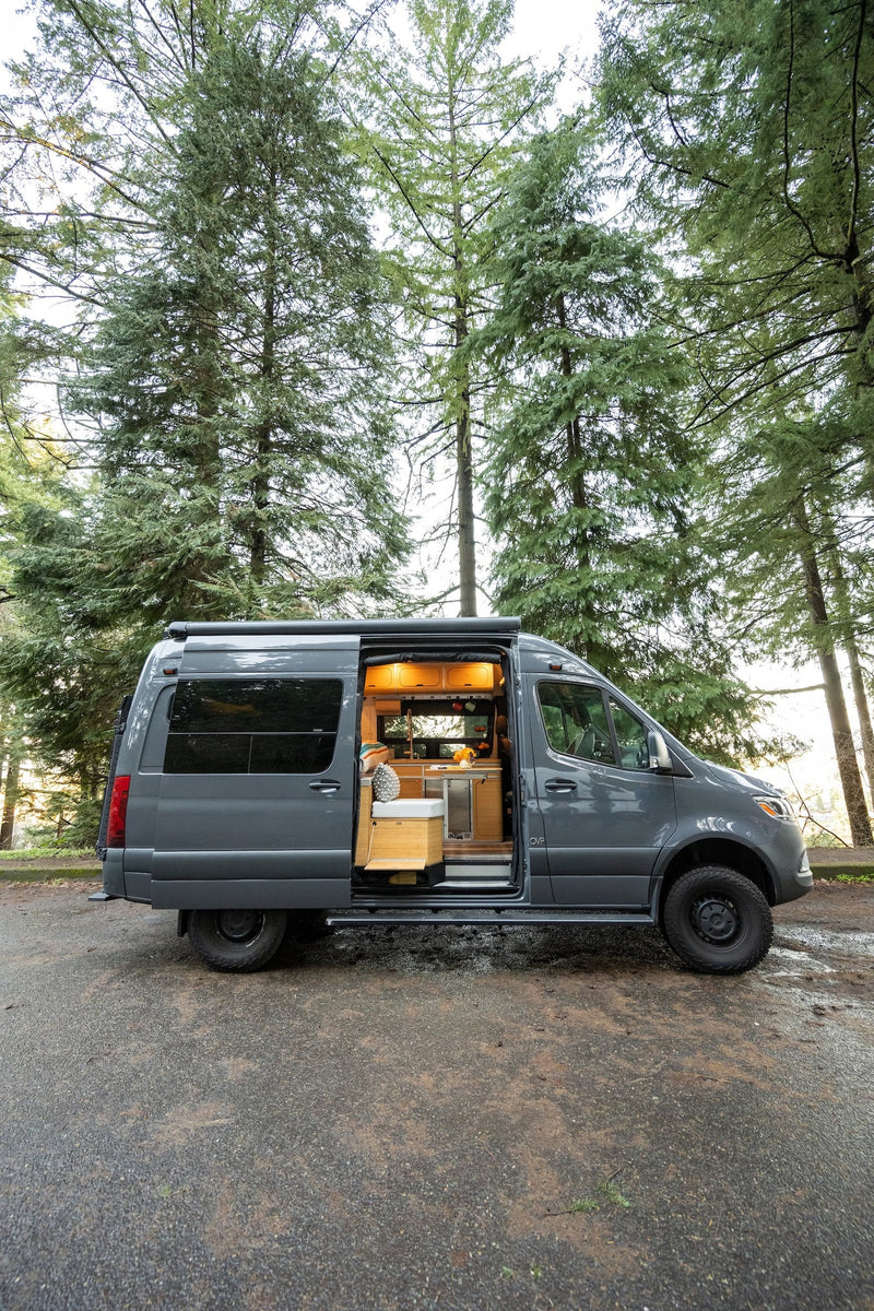 Custom grey camper van RV rental in a lush forest. Side door open — photo 1