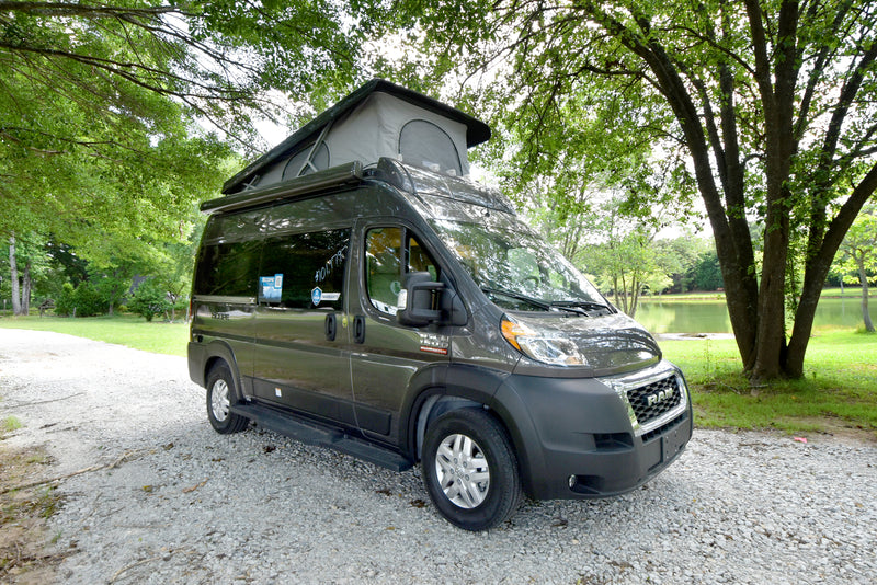 A dark grey Ram ProMaster camper van RV rental with a pop-top roof, parked on a gravel path near a scenic lake. — photo 10