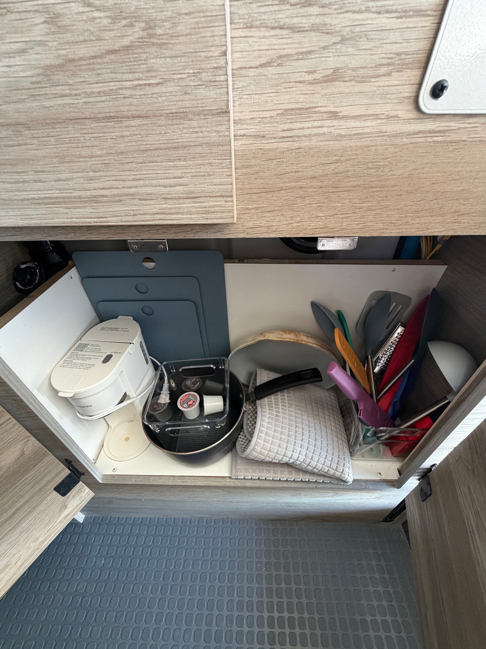 RV rental kitchen: Neatly stored coffee maker, cutting boards, pan, utensils, and K-cups fill this organized cabinet.