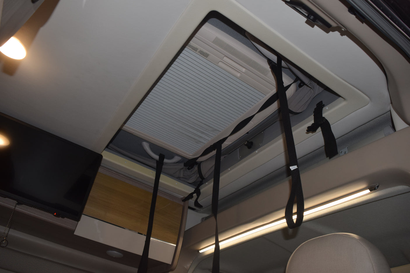 Inside an RV rental: Looking up at a large skylight with AC, mounted TV, and overhead storage cupboards with LED lighting.