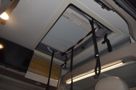 Inside an RV rental: Looking up at a large skylight with AC, mounted TV, and overhead storage cupboards with LED lighting.