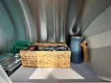 Compact RV rental storage: Woven basket, stacked green containers, and blue bottle in an organized metallic interior.