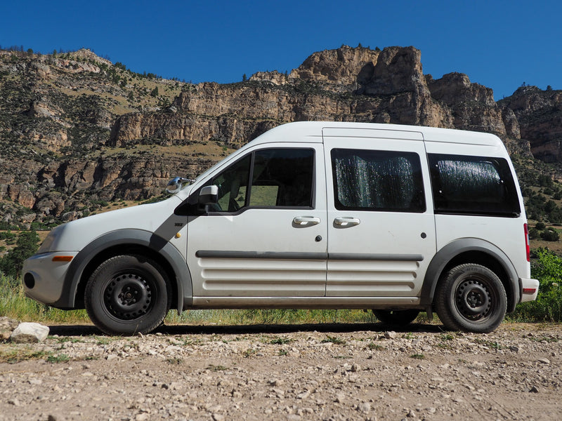 White van for RV rental, parked on a dirt road against rugged mountains under a clear blue sky, ideal for outdoor adventures. — photo 2