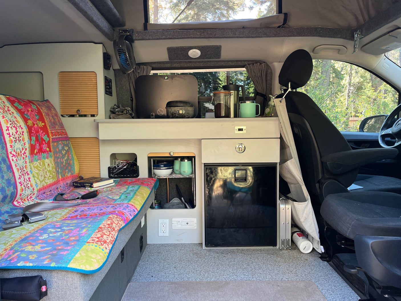 **RV rental** interior: vibrant bed, compact kitchen with fridge, and smart storage solutions for comfortable mobile living.