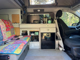 **RV rental** interior: vibrant bed, compact kitchen with fridge, and smart storage solutions for comfortable mobile living.