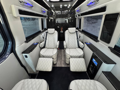 Luxurious custom RV rental interior features four quilted leather captain's chairs, ambient blue lighting, and an entertainment screen.